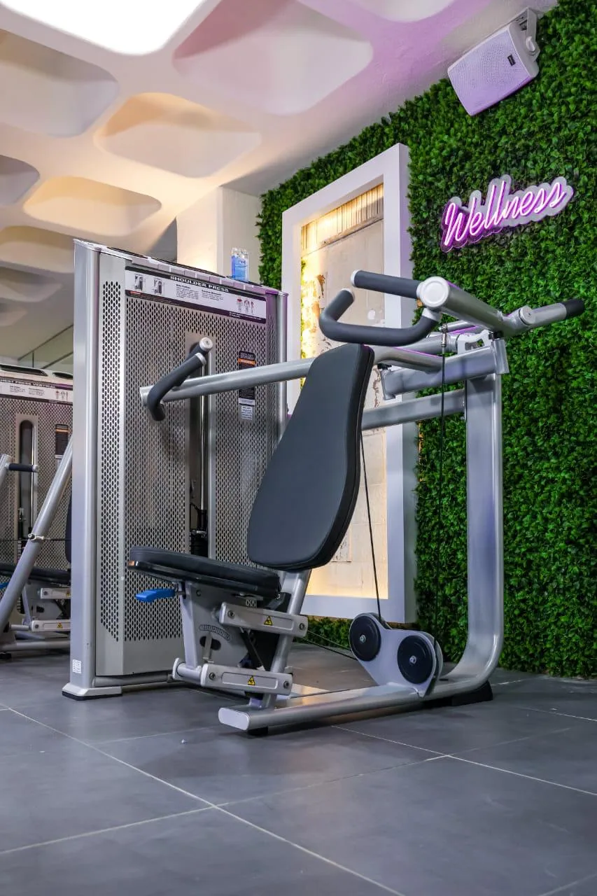 The Wellness corner with a shoulder press machine beside the neon Wellness sign and living green wall